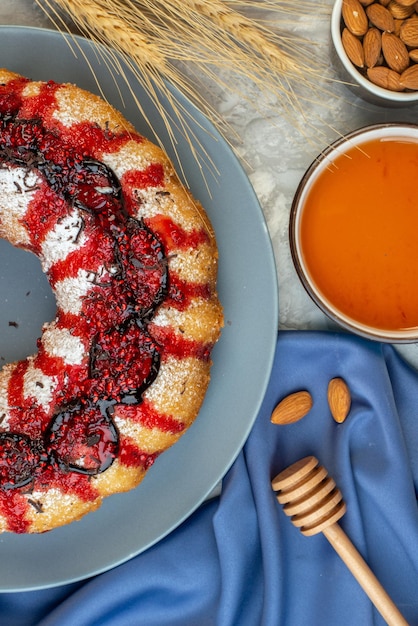 Draufsichtkuchen mit Erdbeere auf rundem Teller Honig in Schüssel Honigstock blauer Schal auf Tisch