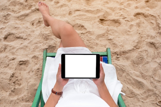 Draufsichtmodell einer Frau, die einen schwarzen Tablet-PC mit leerem Desktop-Bildschirm hält und verwendet, während sie auf einem Strandkorb liegt
