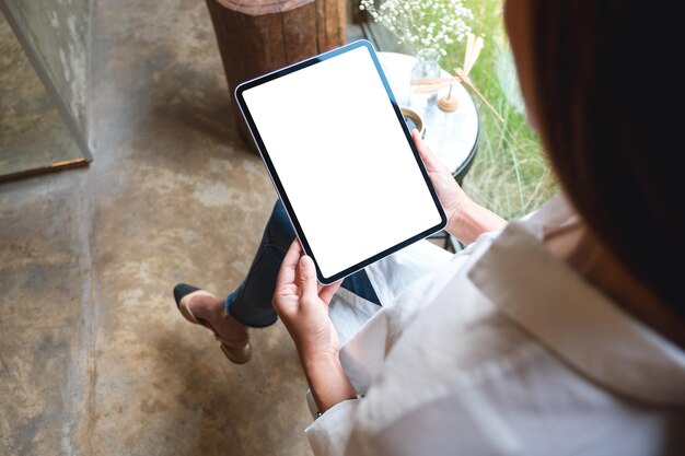 Draufsichtmodellbild einer Frau, die ein digitales Tablet mit einem leeren weißen Desktop-Bildschirm im Café hält