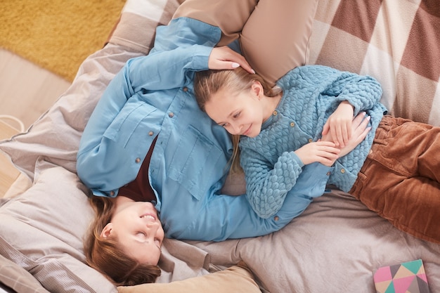 Draufsichtporträt der glücklichen Mutter, die süßes Mädchen umarmt und einander anlächelt, während zu Hause auf Bett liegend, Raum kopieren