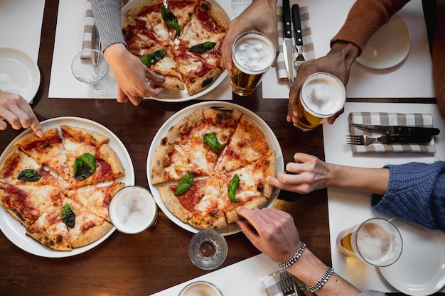 Draufsichttisch mit nicht erkennbarer gemischtrassiger Gruppe mit köstlicher italienischer Pizza und Biergläsern