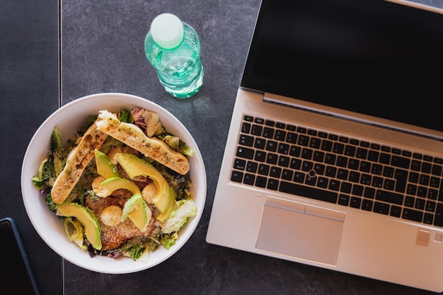 Draufsichttisch mit Salatschüssel Flasche Wasser Computer Laptop und mobile Pause zum Mittagessen Konzept