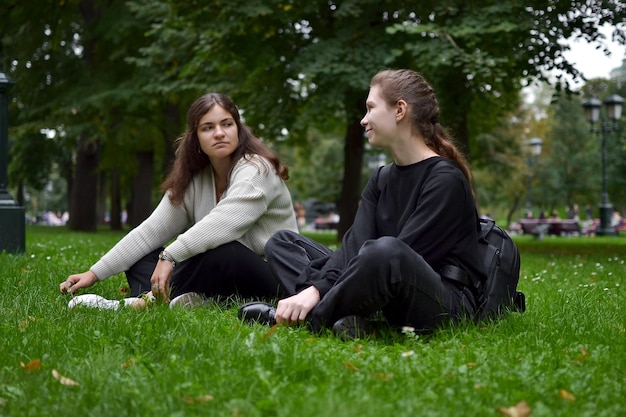 Draußen im Park sitzen zwei junge Frauen auf einer grünen Wiese und unterhalten sich über verschiedene Themen