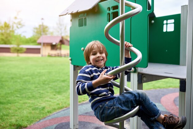 Draußen Porträt des niedlichen Vorschuljungen, der am Spielplatz klettert