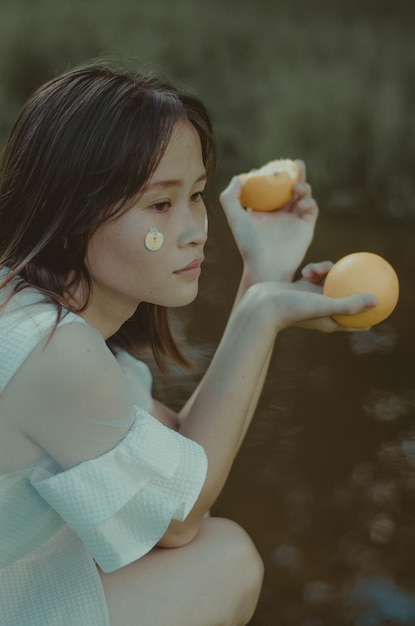 dreamy_young_ethnic_female_eating_orange_near_pond