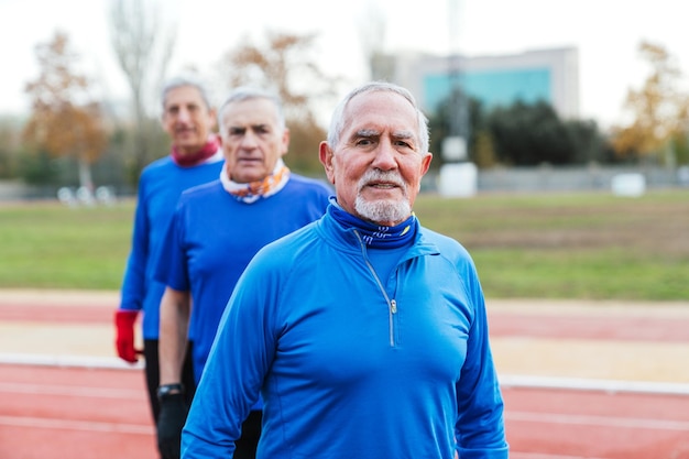 Foto drei ältere männliche läufer in blauer sportkleidung ruhen sich während ihres trainings auf einer außenstrecke aus