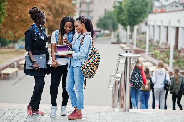 Drei afrikanische Studentinnen posierten mit Rucksäcken und Schulsachen auf dem Hof der Universität und schauten sich Tablet an