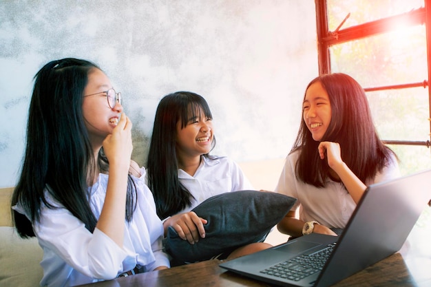 Foto drei asiatische teenager lachen mit glücklichem gesicht, während sie im wohnzimmer an aptop arbeiten