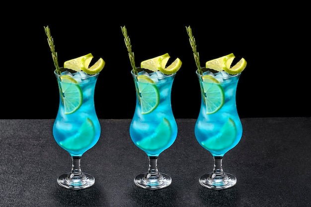 Drei blaue Cocktailgläser verziert mit Zitrone auf schwarzem Hintergrund