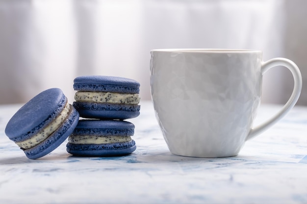 Drei blaue Makronen und eine weiße Tasse auf hellem Hintergrund