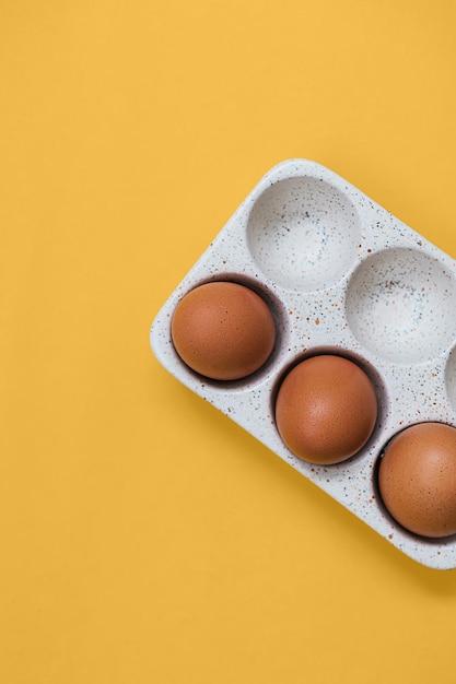 Foto drei braune rohe hühnereier in einem keramischen aufbewahrungsbehälter auf gelbem hintergrund mit kopierraum kreatives osterferiendekor und frühlingsgrüßkarte flachlag