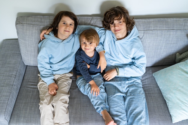 Drei Brüder unterschiedlichen Alters sitzen zu Hause auf einem Sofa. Die älteren Jungen umarmen die jüngeren. Geschwister gute Beziehungen.