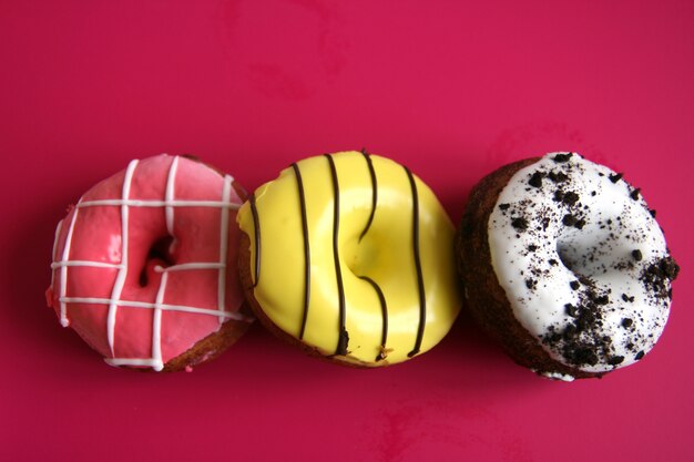 Drei bunte Donuts kaum auf rotem Grund. kopieren sie platz.