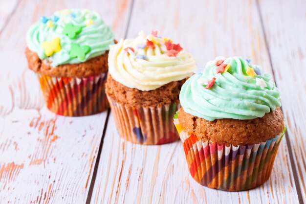 Foto drei bunte handgemachte cupcakes auf einem weißen hölzernen hintergrund.