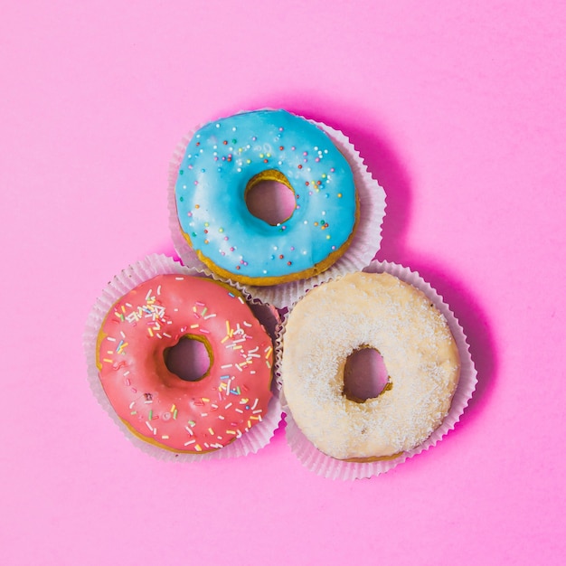 Drei bunte runde Donuts auf rosa Hintergrund