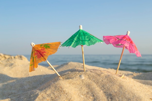 Drei bunte Sonnenschirme aus Papiercocktail am Sandstrand mit blauem Himmel