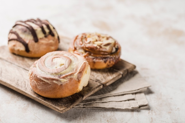 Drei Cinnabon-Brötchen auf einem Holzbrett mit einer Serviette auf einem hellen Hintergrund. Amerikanisches klassisches Brötchen.