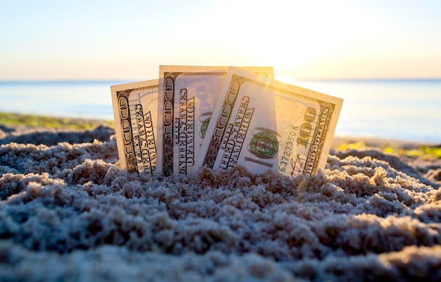 Drei-Dollar-Scheine sind im Sand am Sandstrand in der Nähe des Meeres bei Sonnenuntergang im Morgengrauen begraben