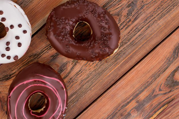 Drei Donuts auf braunem Holzhintergrund. Leckere Kuchen mit Schokoladenglasur. Platz für Text.