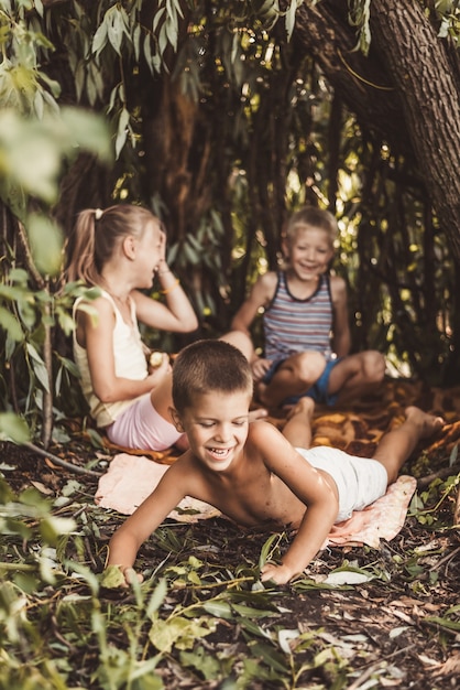 Drei Dorfkinder spielen in einer Hütte, die sie selbst aus Blättern und Zweigen gebaut haben