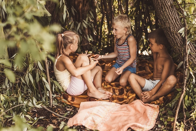 Drei Dorfkinder spielen in einer Hütte, die sie selbst aus Blättern und Zweigen gebaut haben