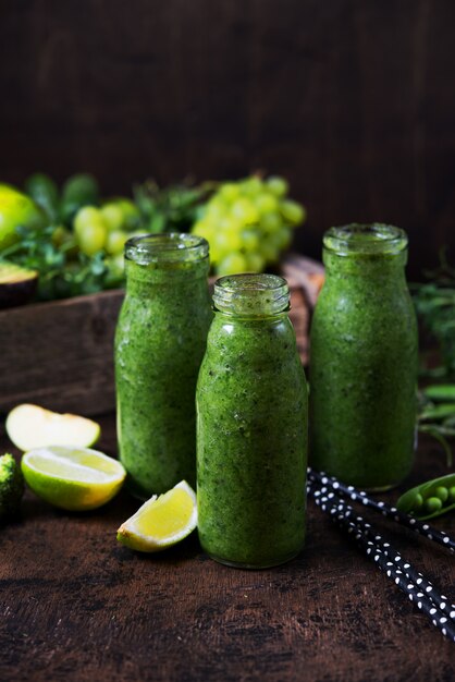 Drei Flaschen des gesündesten grünen Smoothie aus Gemüse und Obst und rund um das grüne Gemüse und Obst. Vertikales Foto. Draufsicht.