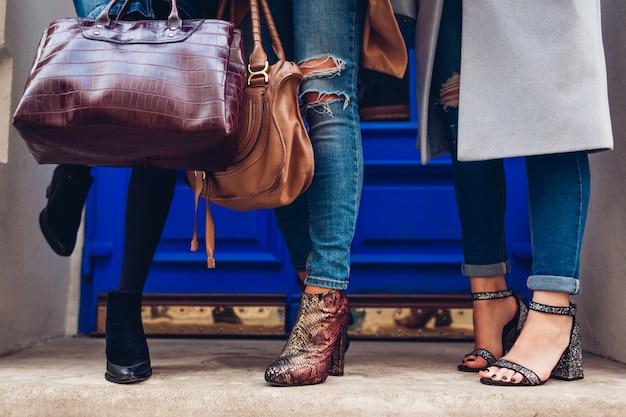 Drei frauen, die draußen stilvolle schuhe und zubehör tragen. beauty-mode-konzept. damen, die weibliche handtaschen halten