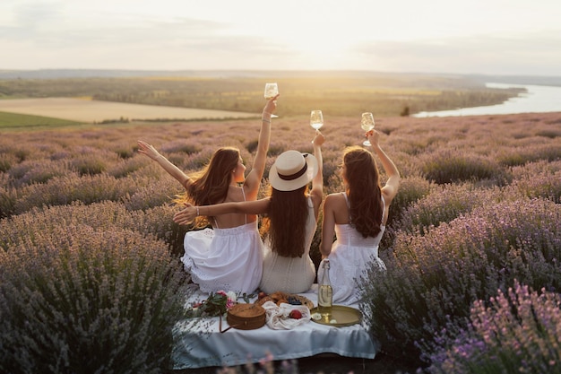 Drei Frauen sitzen auf einer Decke in einem Lavendelfeld und halten Weingläser in der Hand