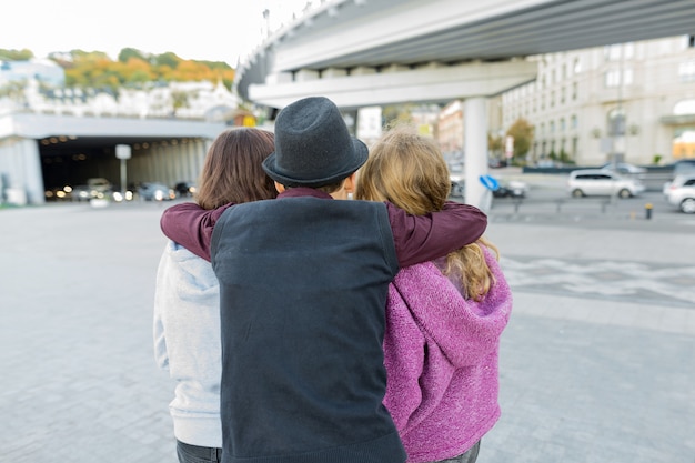 Drei Freunde, Blick von hinten auf einen Jungen, der zwei Mädchen umarmt