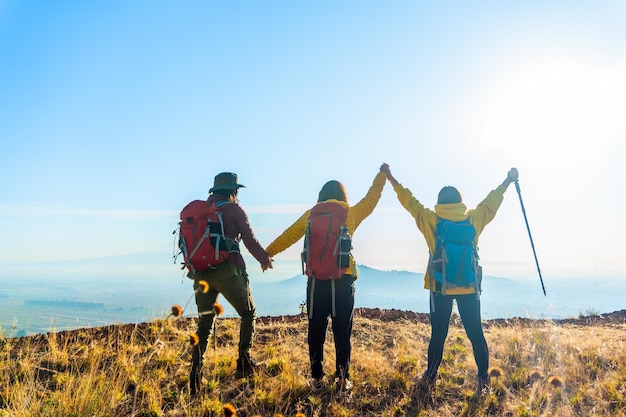 Foto drei freunde in gelben jacken und wanderrucksäcken erreichen die spitze des berges