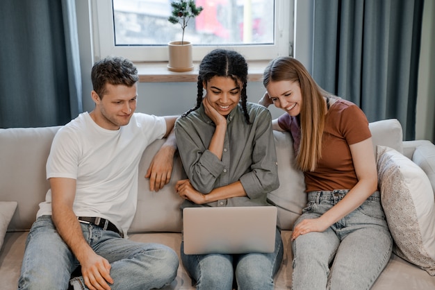 Drei Freunde zu Hause entspannen sich, sitzen auf einem Sofa und lächeln