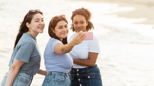 Drei Freundinnen, die Selfie am Strand mit Kopienraum nehmen