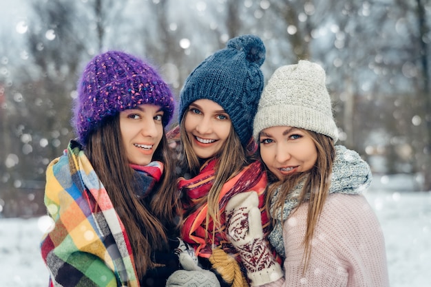 Drei Freundinnen im Freien in Strickmützen, die sich bei schneereichem Wetter amüsieren