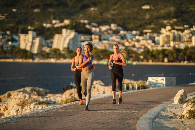 Drei Freundinnen joggen am Meer entlang und genießen den sonnigen Sommertag.