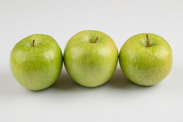 Drei frische grüne Äpfel auf weißem Tisch.
