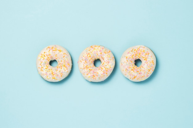 Drei frische köstliche süße Donuts, die in einer Reihe auf einem blauen Hintergrund ausgelegt werden. Fast-Food-Konzept, Bäckerei, Frühstück.