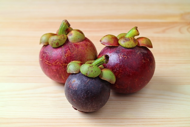 Drei frische reife lila Mangostanfrüchte, bekannt als Königin der Früchte, auf einer Holzoberfläche