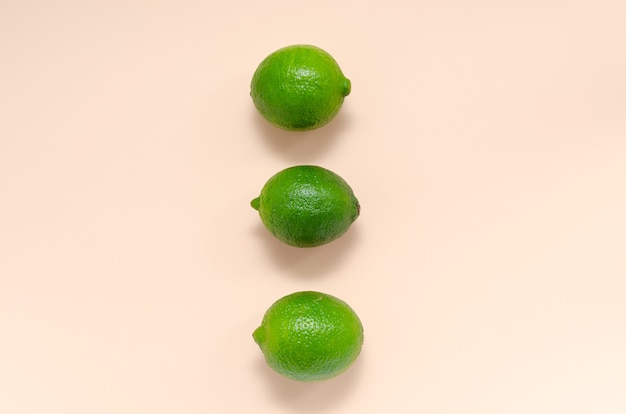 Drei frische saftige helle Limetten auf einem sanften rosa Leuchttisch.