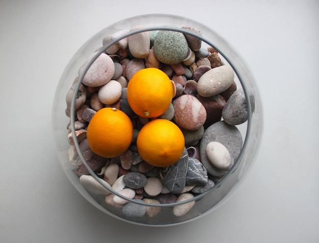 Drei frische Zitronenfrüchte in einer dekorativen Glasvase mit glatten Meeressteinen, Draufsicht
