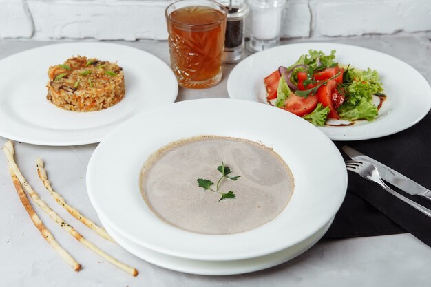 Drei-Gänge-Menü auf einem Tisch in einem Restaurant, Café-Menü. Geschäftsessen von einem Teller mit Pilzcremesuppe, mit Huhn und Ei, einem Salat aus frischem Gemüse und Pilaw.