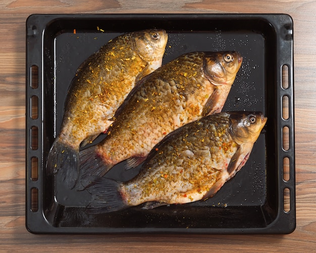 Drei ganze Karausche werden zum Braten im Ofen zubereitet. Der Fisch liegt auf einem Backblech. Frisch gereinigter Fisch mit Gewürzen