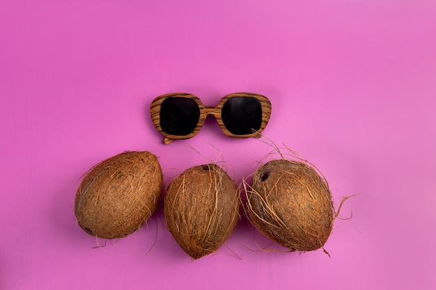 Drei ganze Kokosnüsse und Holzgläser auf rosa Hintergrund.