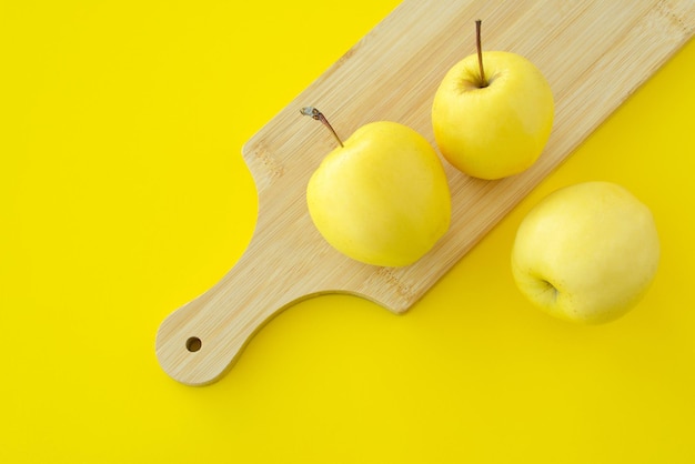 Drei gelbe Äpfel auf einem hölzernen Schneidebrett auf gelbem Hintergrund Frische reife saftige gelbe Früchte