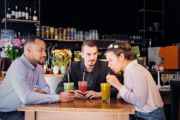 Drei gemischtrassige Freunde trinken erfrischende vegetarische Saftcocktails in einem Café.