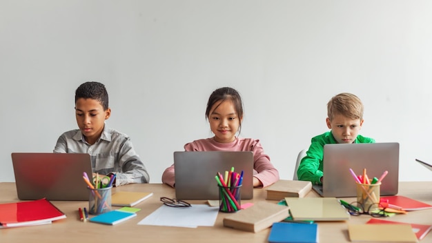 Drei gemischtrassige Schulkinder, die Laptops verwenden, um online in der Schule zu lernen