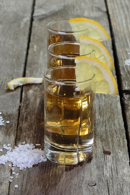 Foto drei gläser tequila mit zitrone und salz auf einem holztisch