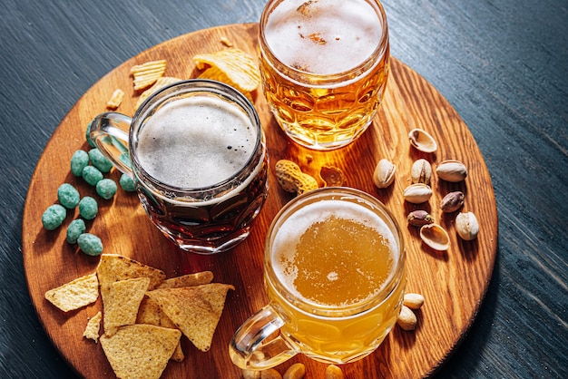 Drei Gläser teures Craft Beer, klassisch und ungefiltert und dunkel in einem Glas auf dem Tisch mit einem Snack aus Erdnuss- und Pistazienchips und Nachos