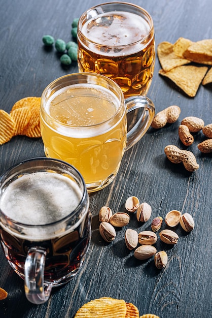 Drei Gläser teures Craft Beer, klassisch und ungefiltert und dunkel in einem Glas auf dem Tisch mit einem Snack aus Erdnuss- und Pistazienchips und Nachos