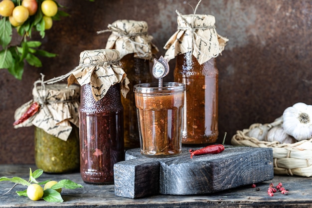 Drei Glasflaschen mit georgischer Tkemali-Sauce mit Zutaten auf rustikalem Holztisch.