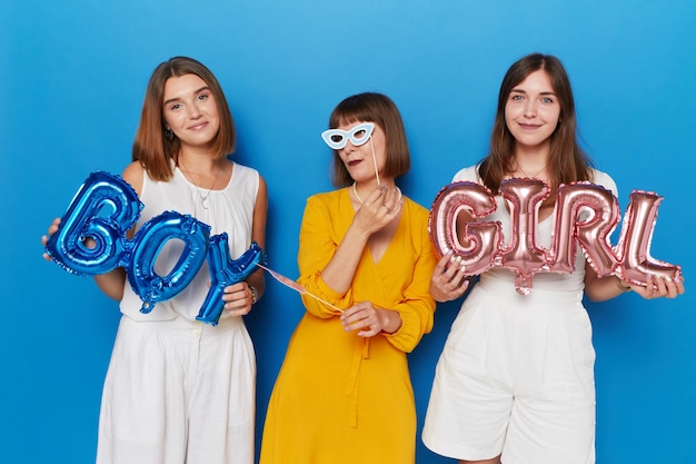 Drei glückliche Frauen, die Geschlecht haben, zeigen einen isolierten blauen Hintergrund. Kopieren Sie Platz